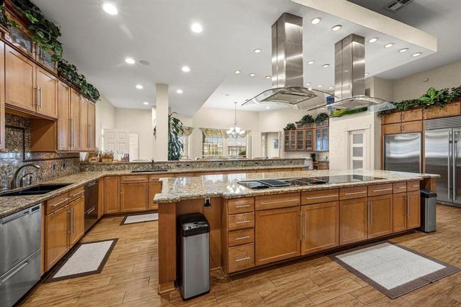 This spacious kitchen features modern stainless steel appliances, ample wooden cabinetry, granite countertops, and a large island. It's well-lit with a combination of recessed and pendant lighting, and offers an open layout with a view into the adjoining living spaces. | Image 10