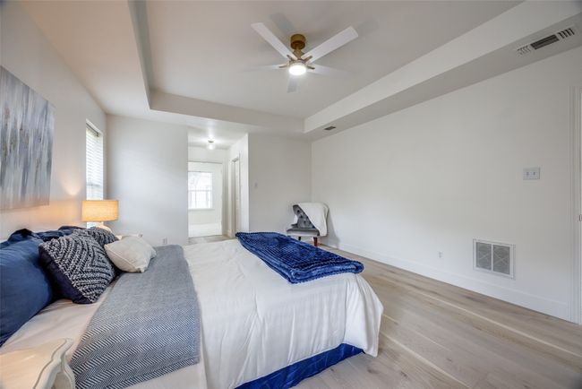 Bedroom featuring light wood finished floors, a raised ceiling, and ceiling fan | Image 17