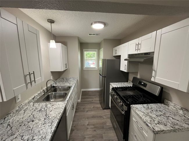 Kitchen featuring appliances with stainless steel finishes, a sink, under cabinet range hood, dark wood finished floors, and white cabinetry | Image 6
