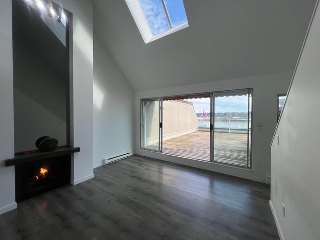 Unfurnished living room with vaulted ceiling, dark wood-type flooring, a skylight, a water view, and a lit fireplace | Image 4