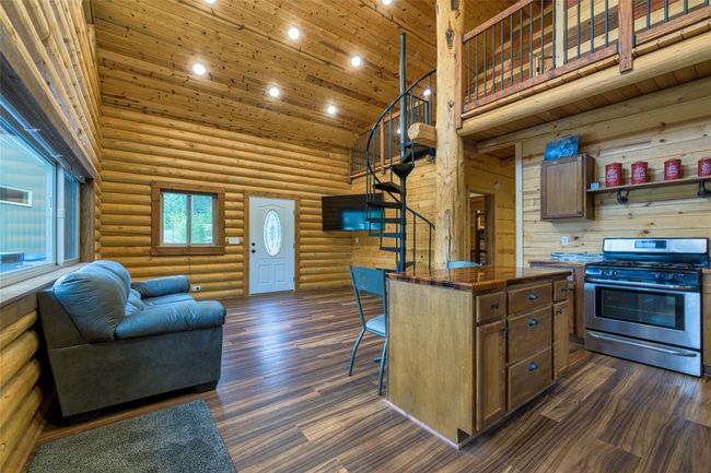 Kitchen featuring high vaulted ceiling, rustic walls, stainless steel gas range oven, open floor plan, and dark wood-style floors | Image 6