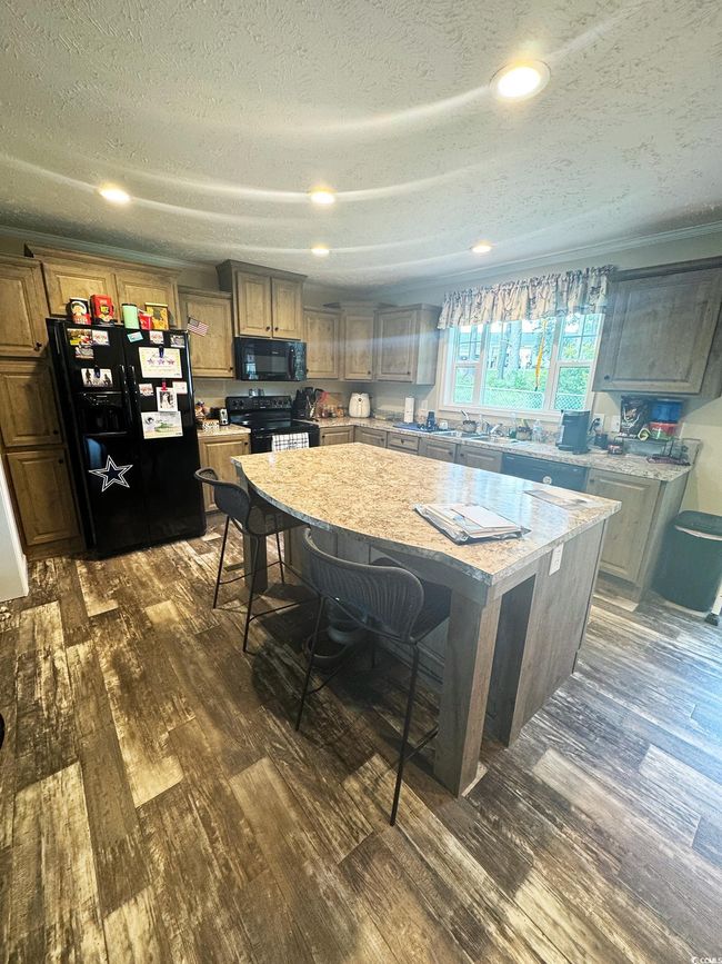 Kitchen with dark wood finished floors, black appliances, a center island, a breakfast bar area, and a textured ceiling | Image 13