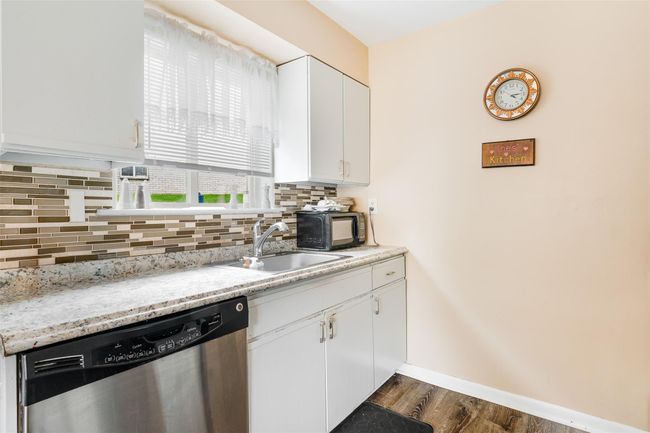 Kitchen featuring stainless steel dishwasher, backsplash, dark wood-type flooring, and black microwave | Image 9