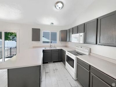 Kitchen with light hardwood / wood-style flooring, white appliances, vaulted ceiling, and sink | Image 2