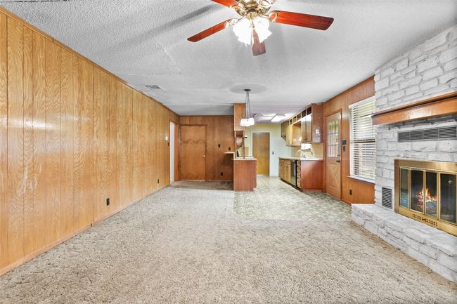 Unfurnished living room with wooden walls, ceiling fan, a textured ceiling, a stone fireplace, and light carpet | Image 16