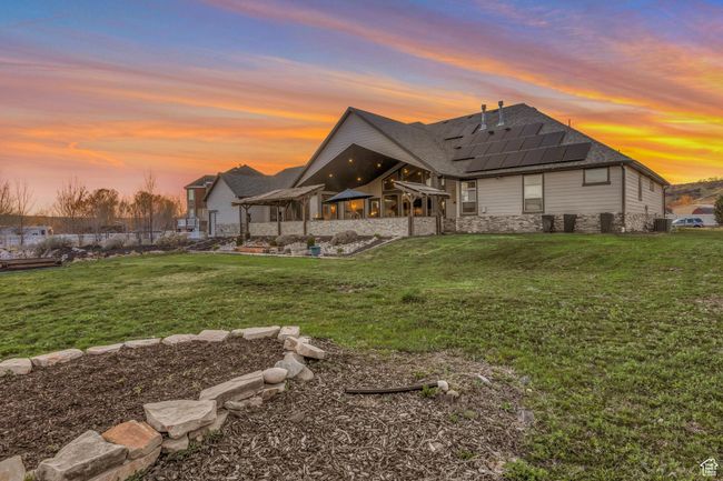 Back of house at dusk featuring roof mounted solar panels, stone siding, a lawn, cooling unit, and a patio | Image 37