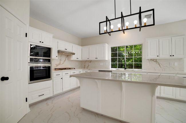 Kitchen with stainless steel appliances, light marble finish floors, backsplash, and white cabinets | Image 6