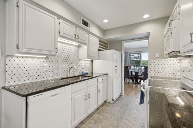 Kitchen featuring white appliances, a sink, white cabinetry, dark stone counters, and recessed lighting | Image 14