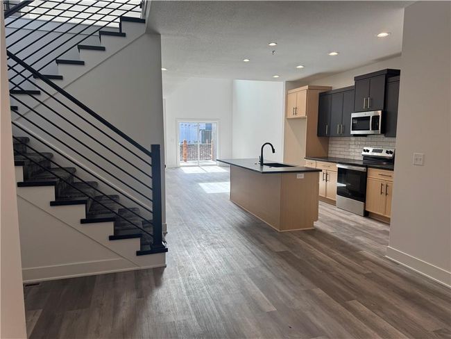 Kitchen with a sink, dark wood finished floors, stainless steel appliances, dark countertops, and decorative backsplash | Image 5