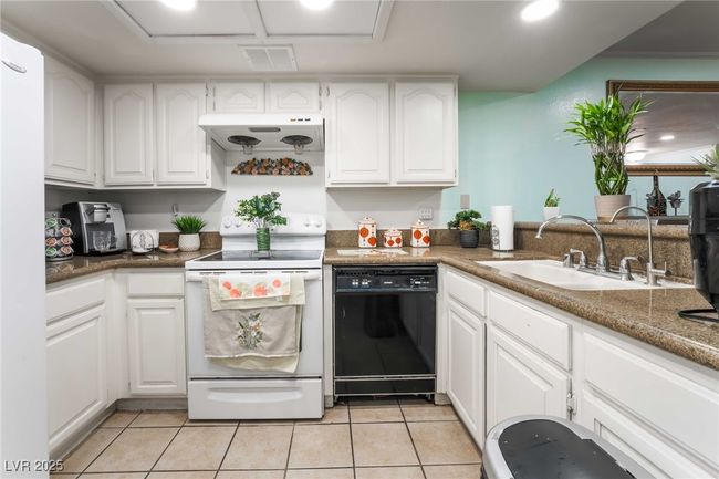 Kitchen featuring white range with electric cooktop, under cabinet range hood, dishwasher, a sink, and visible vents | Image 14