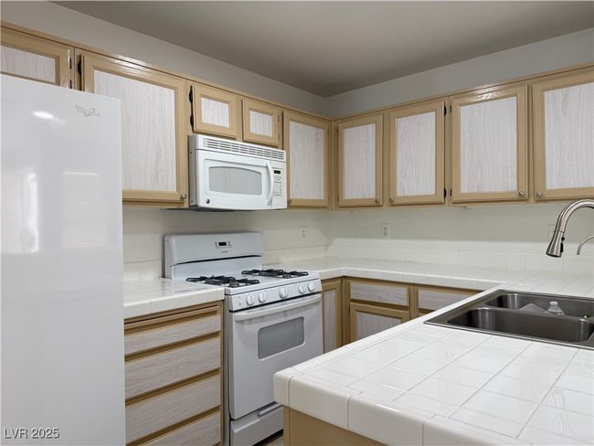 Kitchen featuring light brown cabinets, a sink, tile countertops, white appliances, and glass insert cabinets | Image 20