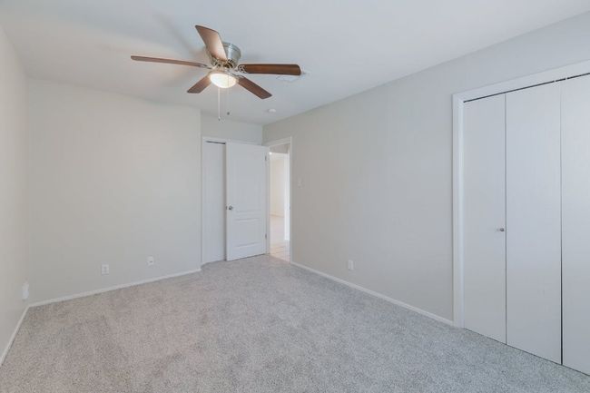 Unfurnished bedroom with carpet flooring, baseboards, two closets, and ceiling fan | Image 4