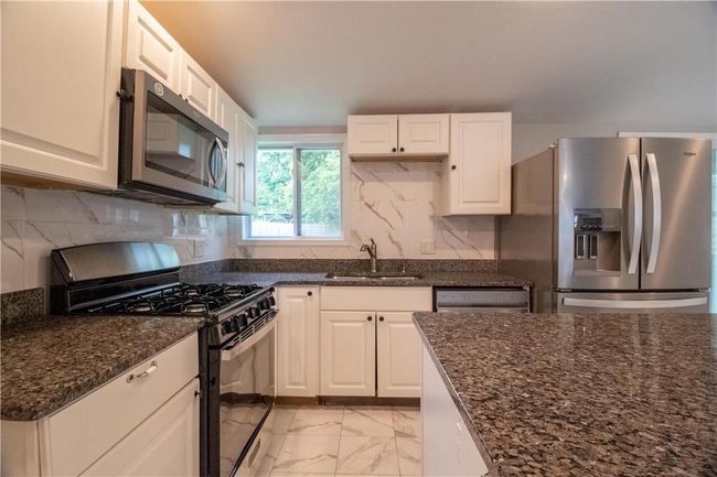 Kitchen featuring white cabinetry, light tile patterned floors, appliances with stainless steel finishes, decorative backsplash, and sink | Image 7