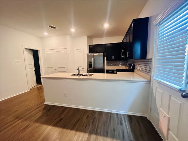 Kitchen featuring stainless steel refrigerator with ice dispenser, dark cabinets, dark wood-style floors, light countertops, and recessed lighting | Image 4