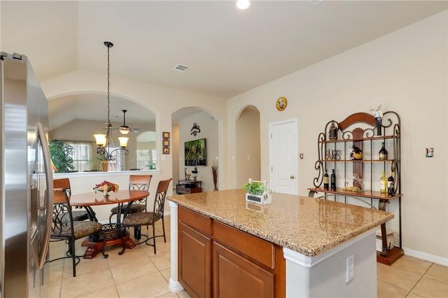 Kitchen with stainless steel fridge with ice dispenser, light tile patterned floors, light stone countertops, a center island, and hanging light fixtures | Image 6