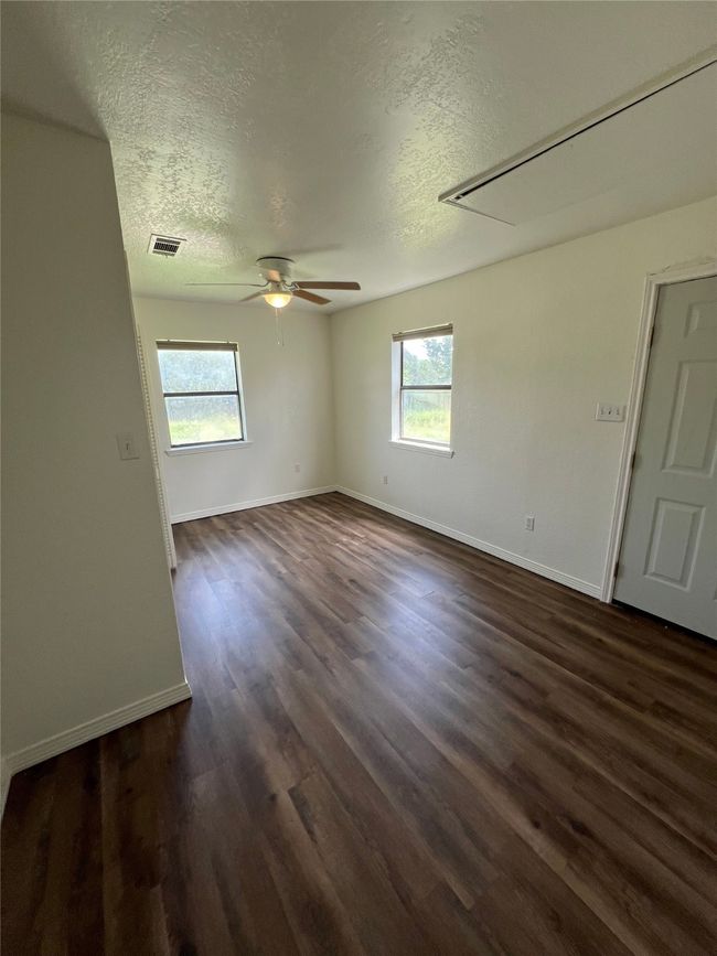 Unfurnished room featuring a textured ceiling, healthy amount of natural light, dark wood finished floors, ceiling fan, and attic access | Image 6