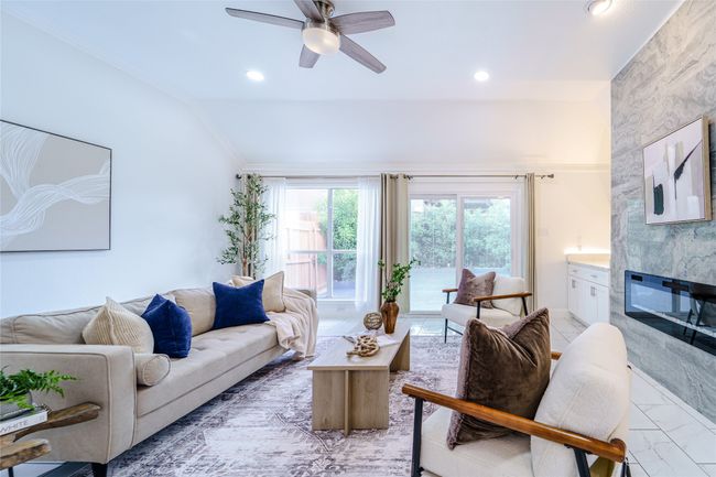 Living room featuring vaulted ceiling, a fireplace, a ceiling fan, ornamental molding, and light marble finish flooring | Image 13