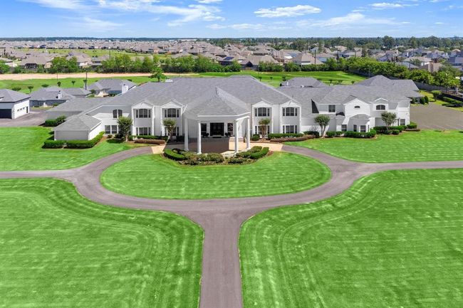 This is an aerial view of a spacious 2 story home with a symmetric facade, well-manicured lawns, and a circular driveway, set in a suburban style neighborhood with similar upscale houses. | Image 4