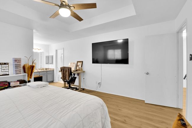 Bedroom featuring a raised ceiling, light wood-style flooring, an office area, connected bathroom, and a ceiling fan | Image 19