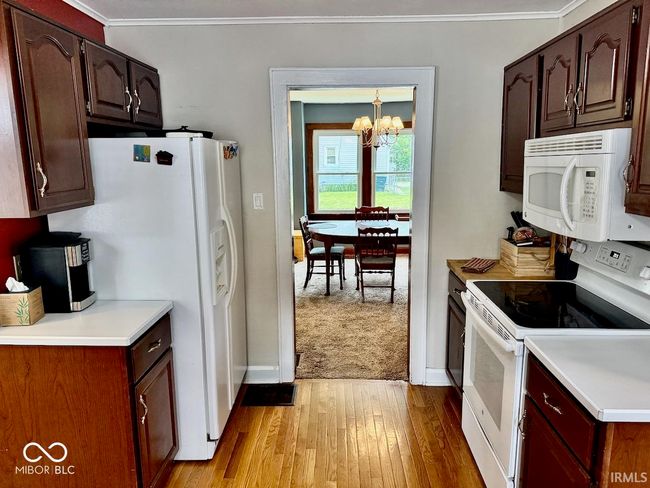 kitchen featuring white appliances, a chandelier, ornamental molding, light wood-style flooring, and light countertops | Image 20
