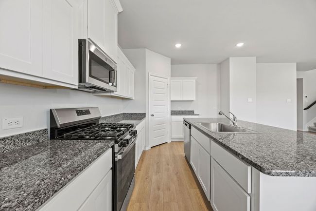Kitchen with stainless steel appliances, light wood finished floors, a kitchen island with sink, white cabinetry, and dark stone counters | Image 7