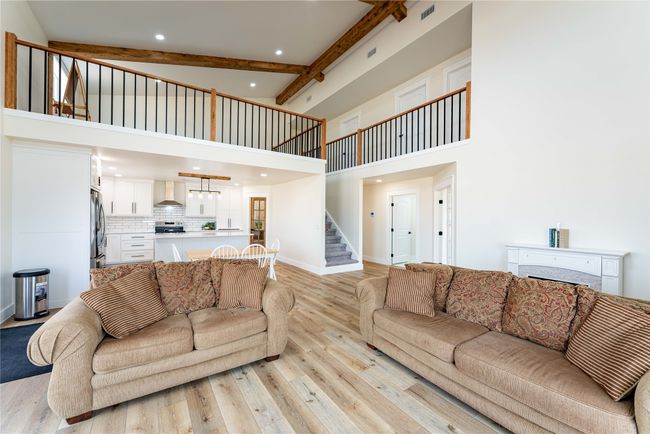 Living room featuring a high ceiling, baseboards, stairs, light wood-style floors, and beamed ceiling | Image 7