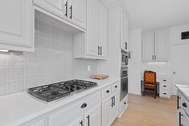 Kitchen featuring stainless steel appliances, decorative backsplash, light countertops, and white cabinets | Image 12