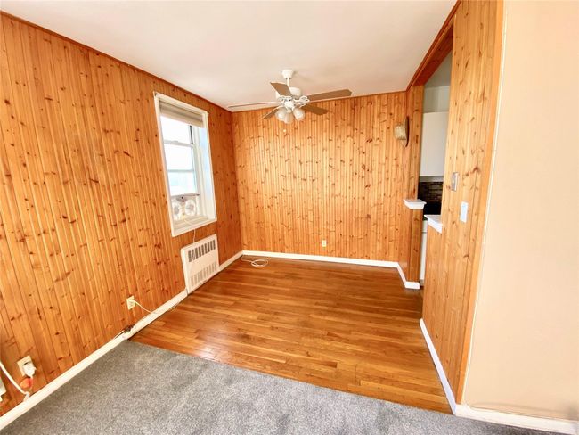 Unfurnished room featuring radiator, ceiling fan, wooden walls, and wood finished floors | Image 9