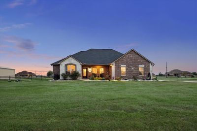 This is a single-story brick home with a well-maintained lawn, featuring a spacious yard and a welcoming entrance, set against a beautiful twilight sky. | Image 1