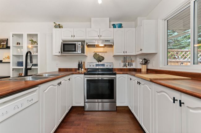 Kitchen featuring stainless steel appliances, under cabinet range hood, white cabinetry, and dark wood-type flooring | Image 4