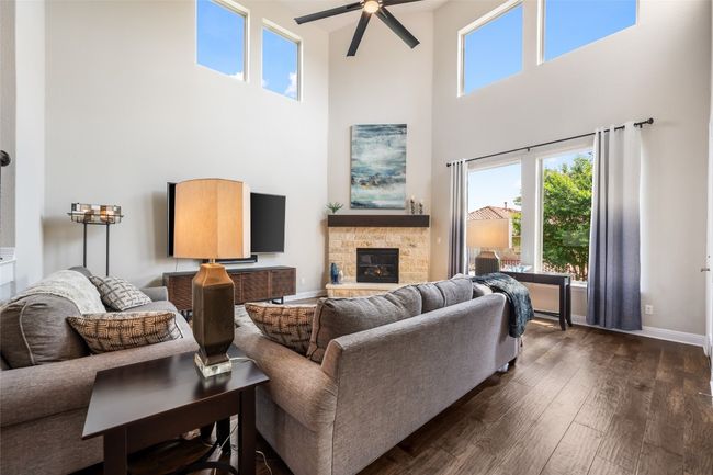 Living area featuring a towering ceiling, dark wood finished floors, ceiling fan, a stone fireplace, and healthy amount of natural light | Image 9