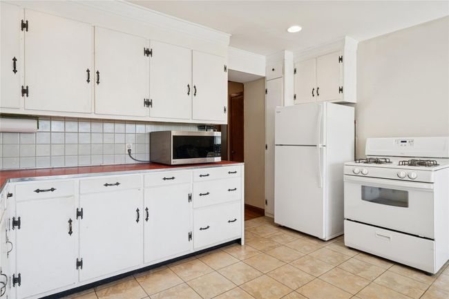 Kitchen with white appliances, light tile patterned floors, decorative backsplash, light countertops, and white cabinets | Image 20