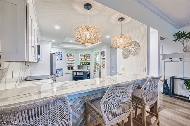 Kitchen featuring light stone counters, light wood-style floors, a peninsula, pendant lighting, and ornamental molding | Image 13