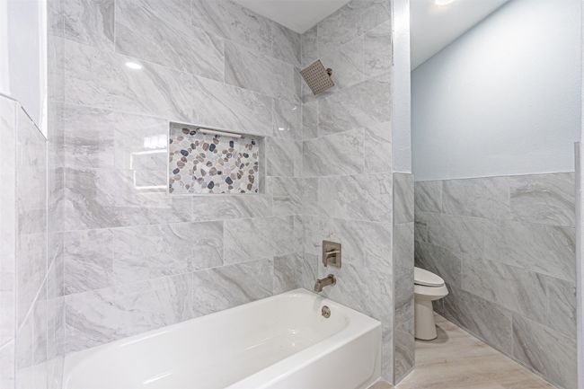 Bathroom featuring tile walls, shower combination, and toilet | Image 25