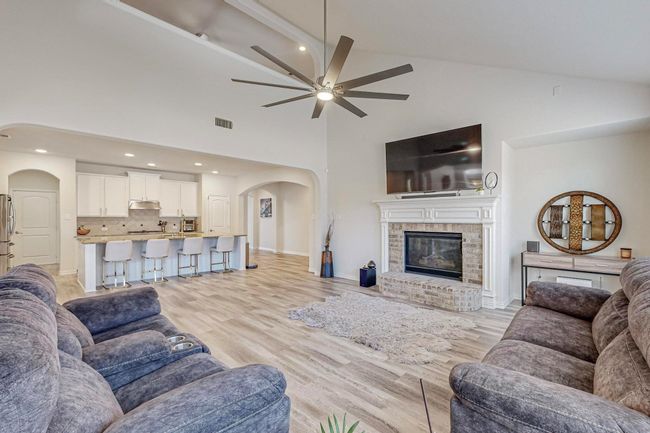 Living area featuring arched walkways, ceiling fan, high vaulted ceiling, light wood-style floors, and a brick fireplace | Image 25
