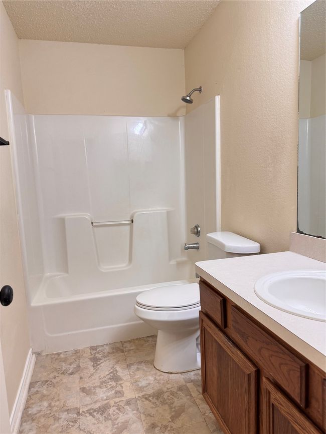 Full bathroom featuring toilet, a textured ceiling, vanity, and washtub / shower combination | Image 14