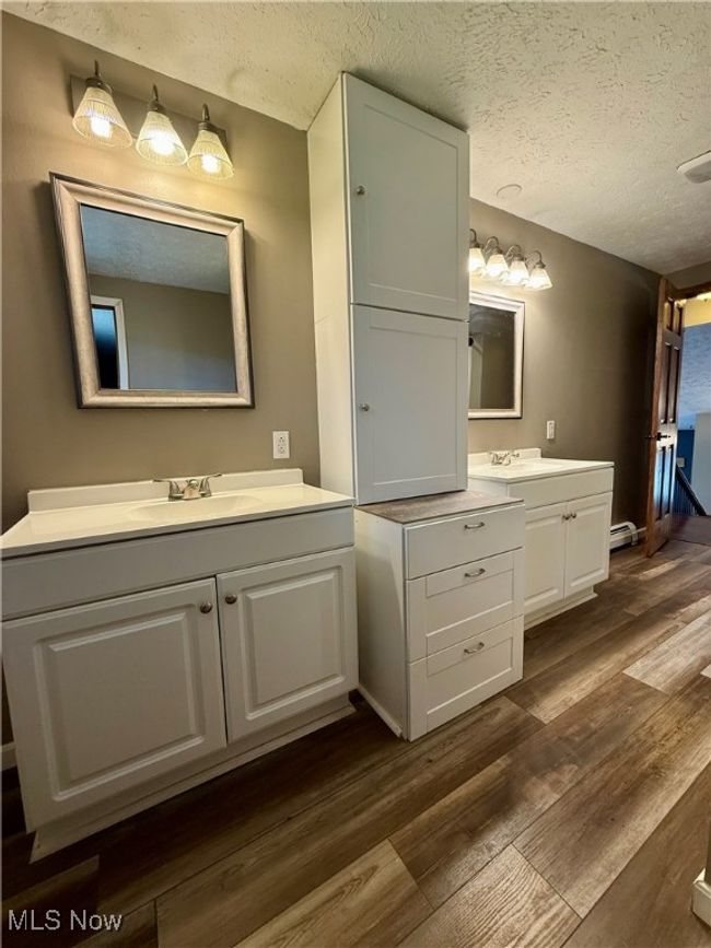 Bathroom with a textured ceiling, wood finished floors, two vanities, and a sink | Image 24