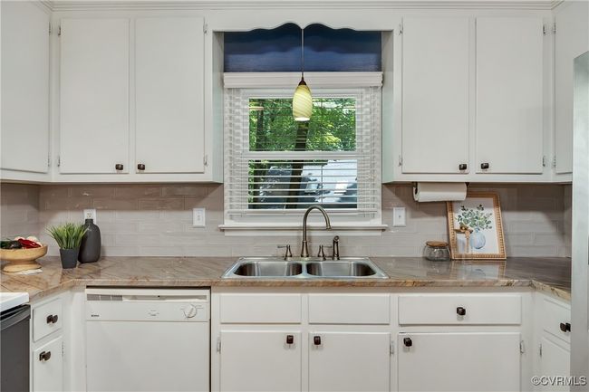 Updated kitchen featuring white dishwasher, white cabinetry, quartzite countertops, backsplash, custom built-in pantry & bar area, new lighting | Image 15