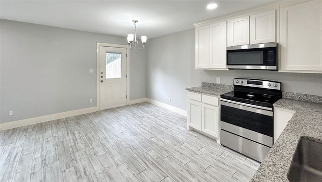 Kitchen featuring stainless steel appliances, a chandelier, white cabinetry, and light wood-style floors | Image 6