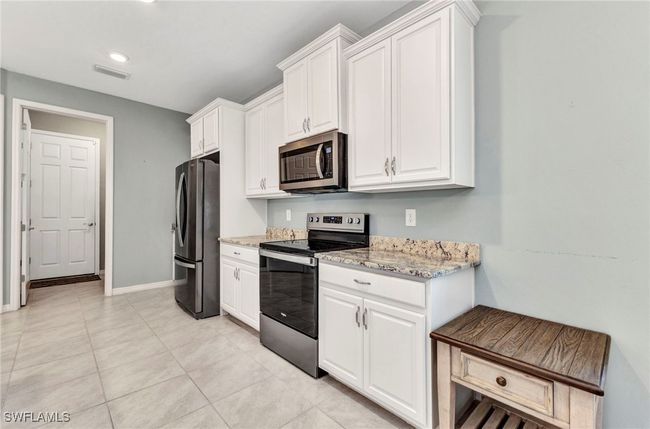 Kitchen with light tile patterned floors, white cabinets, visible vents, appliances with stainless steel finishes, and light stone counters | Image 24