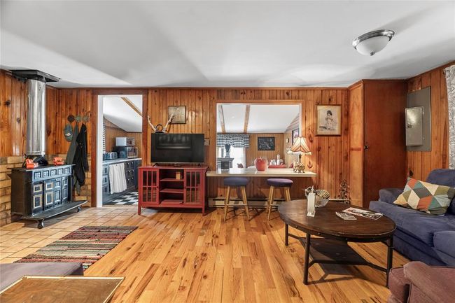Living room featuring a wood stove, baseboard heating, wooden walls, electric panel, and light wood-type flooring | Image 9