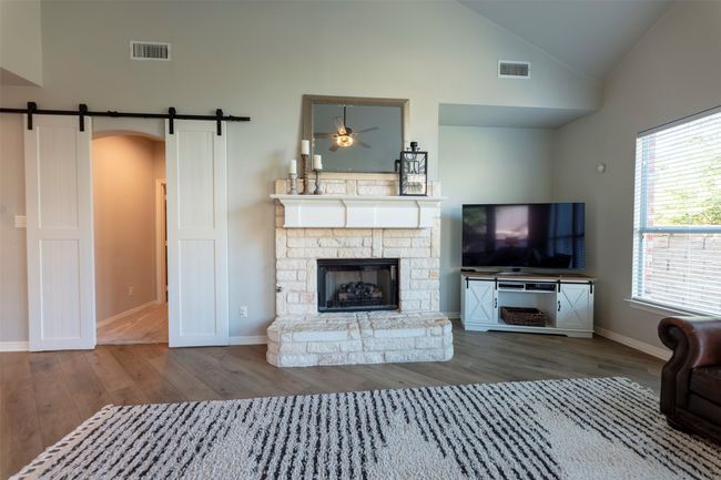 Unfurnished living room with a barn door, wood finished floors, high vaulted ceiling, a fireplace, and a ceiling fan | Image 12