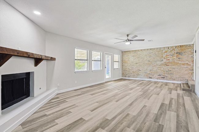 Unfurnished living room with a fireplace with raised hearth, a ceiling fan, light wood-style floors, and baseboards | Image 20