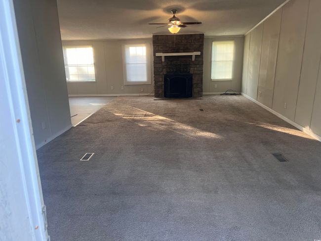 Unfurnished living room featuring a ceiling fan, healthy amount of natural light, carpet flooring, and a stone fireplace | Image 4