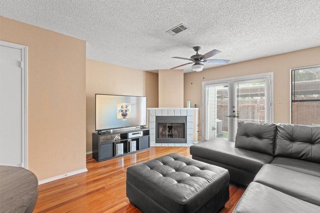 Living room with light wood finished floors, a ceiling fan, a textured ceiling, and a fireplace | Image 4