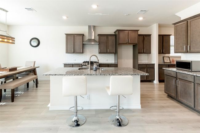 Kitchen featuring a breakfast bar, light stone countertops, decorative backsplash, a kitchen island with sink, and stainless steel microwave | Image 10