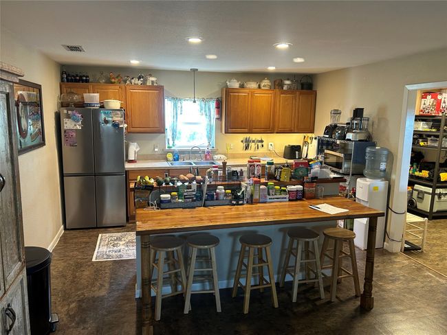 Kitchen featuring freestanding refrigerator, a kitchen bar, brown cabinets, a kitchen island, and recessed lighting | Image 15