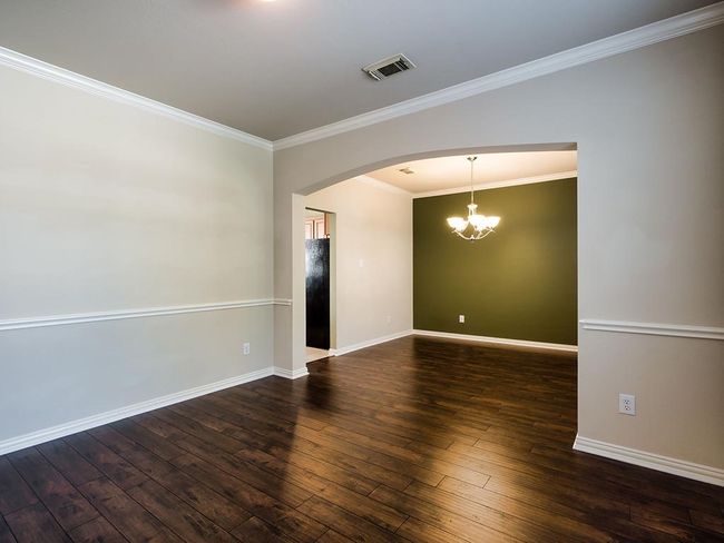 Spare room with arched walkways, hardwood / wood-style flooring, a chandelier, crown molding, and baseboards | Image 9