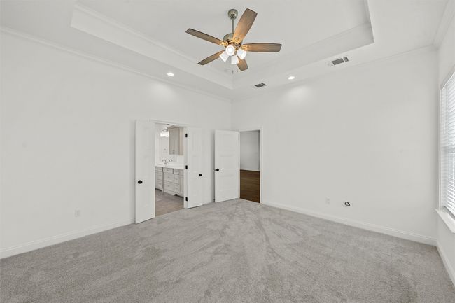 Unfurnished bedroom with a raised ceiling, ornamental molding, carpet, ensuite bathroom, and multiple windows | Image 22