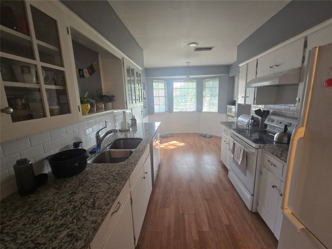 Kitchen featuring white appliances, wood finished floors, tasteful backsplash, and white cabinets | Image 9